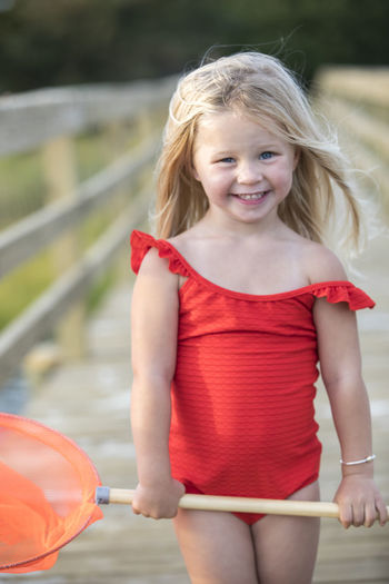 Little girl in red bathing suit on bridge holding red fishing net