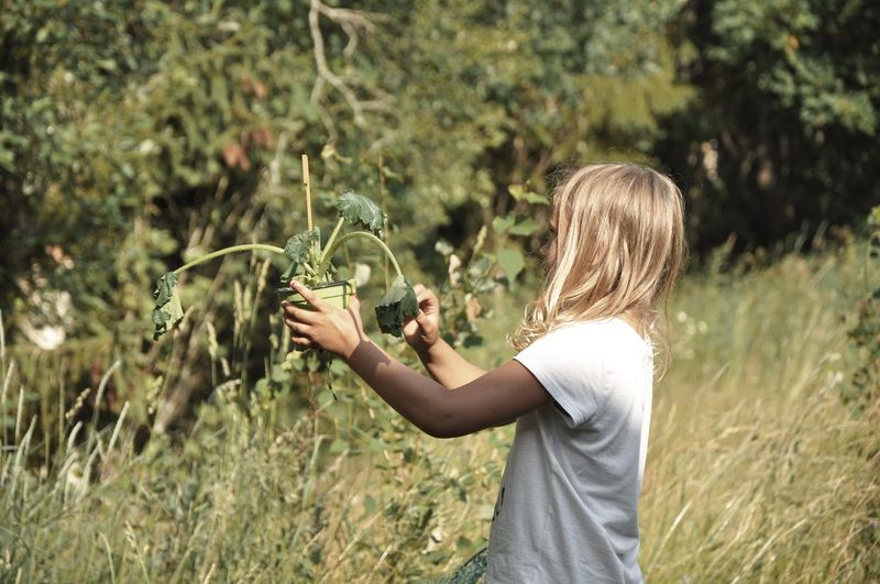 Side view of girl holding plant on field