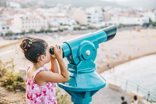 Girl looking the beach through a telescope