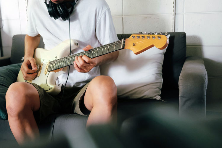 Man playing guitar while sitting on sofa at home