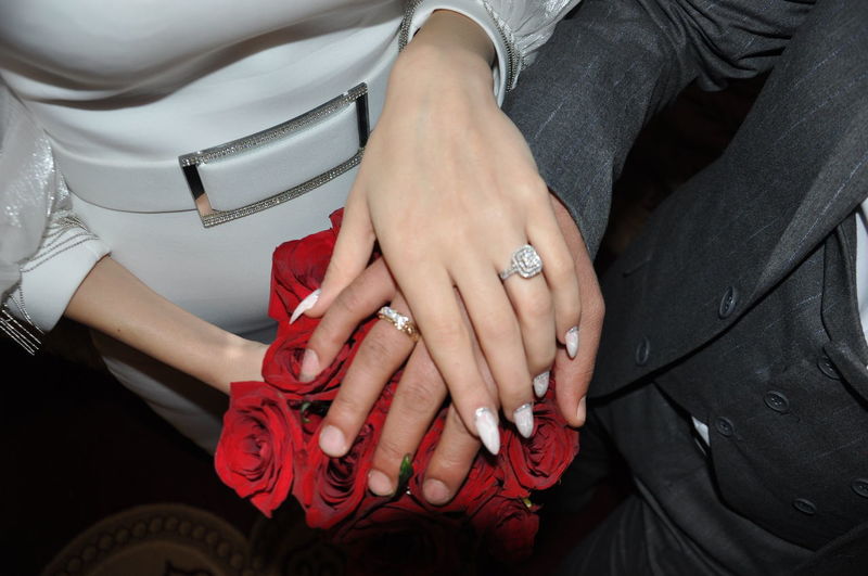 Wedding rings and bouquet of red roses in the hands of the bride and groom