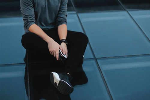 Low section of man holding mobile phone while sitting on floor