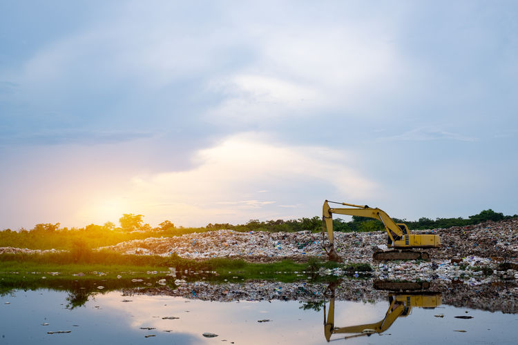 A yellow backhoe is lifting garbage at waste separation plant