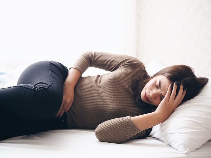 Woman with stomachache lying down on bed at home