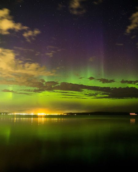 Aurora borealis over sea with reflection against cloudy sky at night
