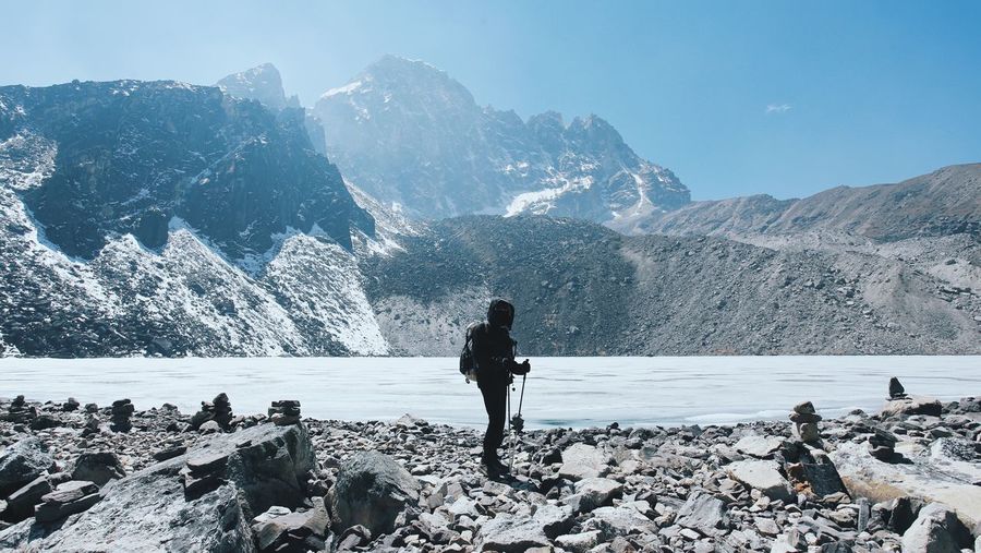 Person standing by gokyo lake against rocky mountains on sunny day