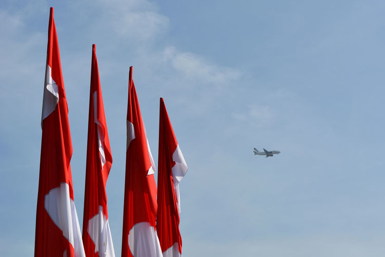 Low angle view of flags and airplane flying against sky
