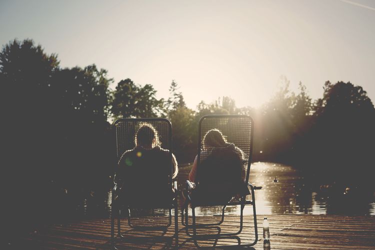 Rear view of silhouette friends sitting on chairs against clear sky at park