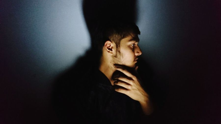 Side view of thoughtful young man looking away while standing by wall in darkroom