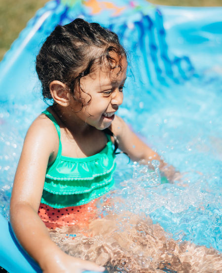 Mixed race young girl at home having fun on hot summer day in kiddie pool