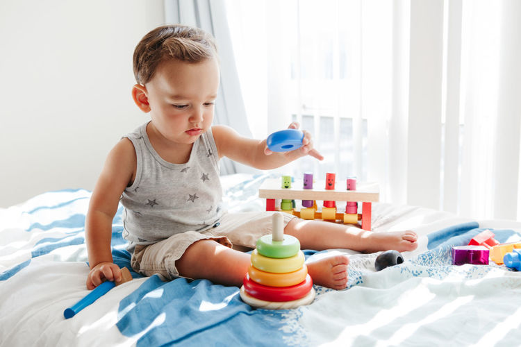 Toddler playing with learning toy pyramid stacking blocks at home. early age montessori education