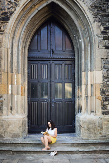 Full length of woman sitting against door outdoors