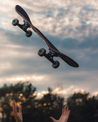 Close-up of hand catching skateboard against sky during sunset