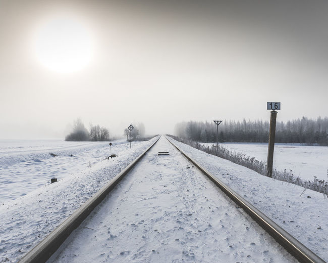 Snow covered railroad track against sky during sunset