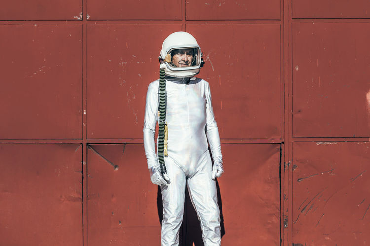 Man in spacesuit standing near red wall of industrial facility on sunny day