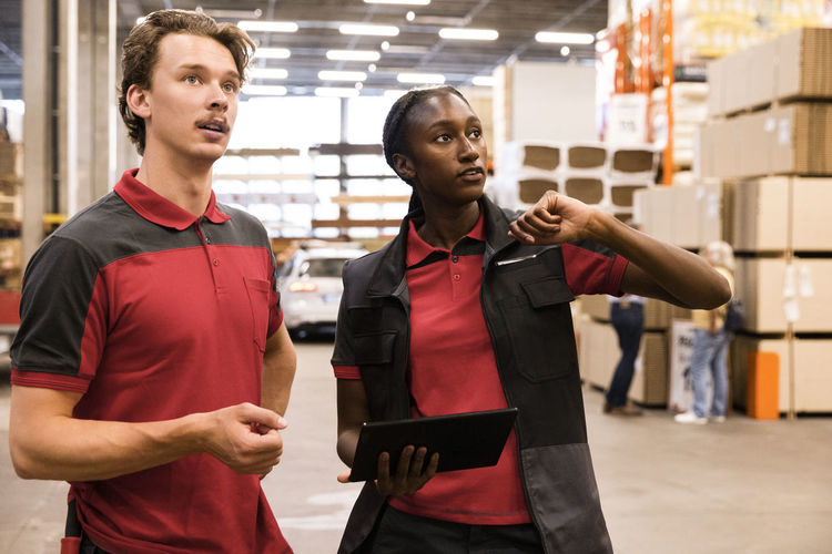 Saleswoman holding digital tablet while discussing with male staff at hardware store