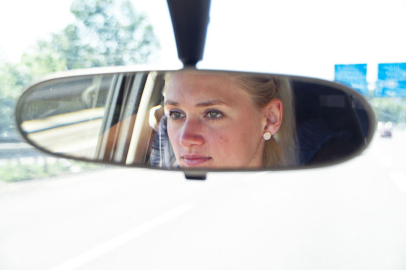 Young woman reflecting on rear-view mirror in car