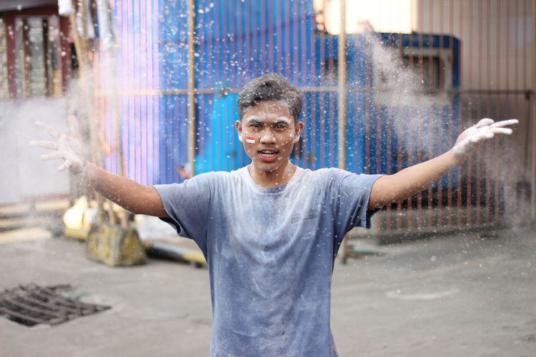 Portrait of man throwing power paint while standing in city
