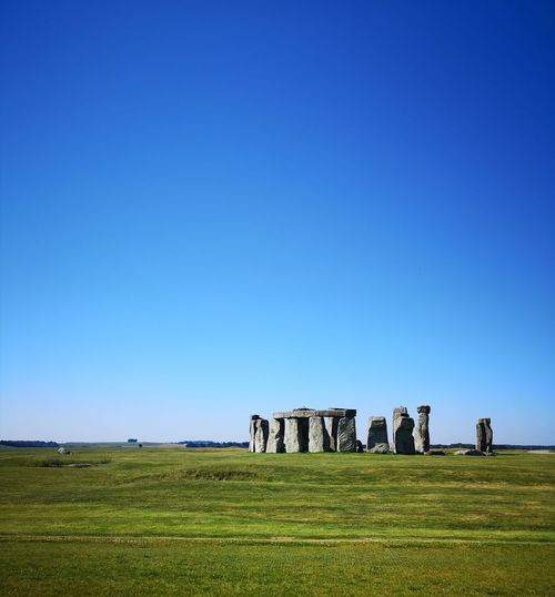 Ancient stonehenge on field against clear blue sky