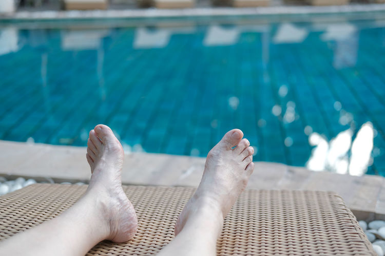 Low section of person relaxing at swimming pool