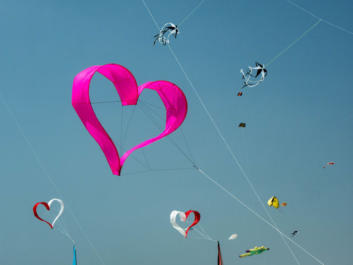 Low angle view of kites flying against clear blue sky
