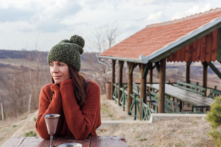 Smiling woman looking away with drink in container on table during winter