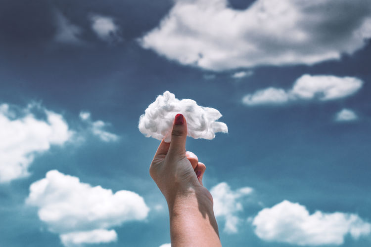 Cropped hand of woman holding cotton against cloudy sky