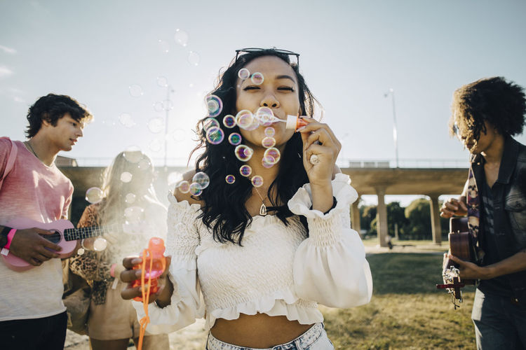 Woman blowing soap bubbles while friends playing ukulele during music event