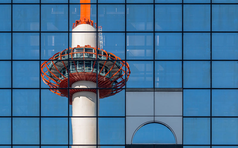 Full frame reflected view of a modern tower against a glass mirrored building against clear blue sky