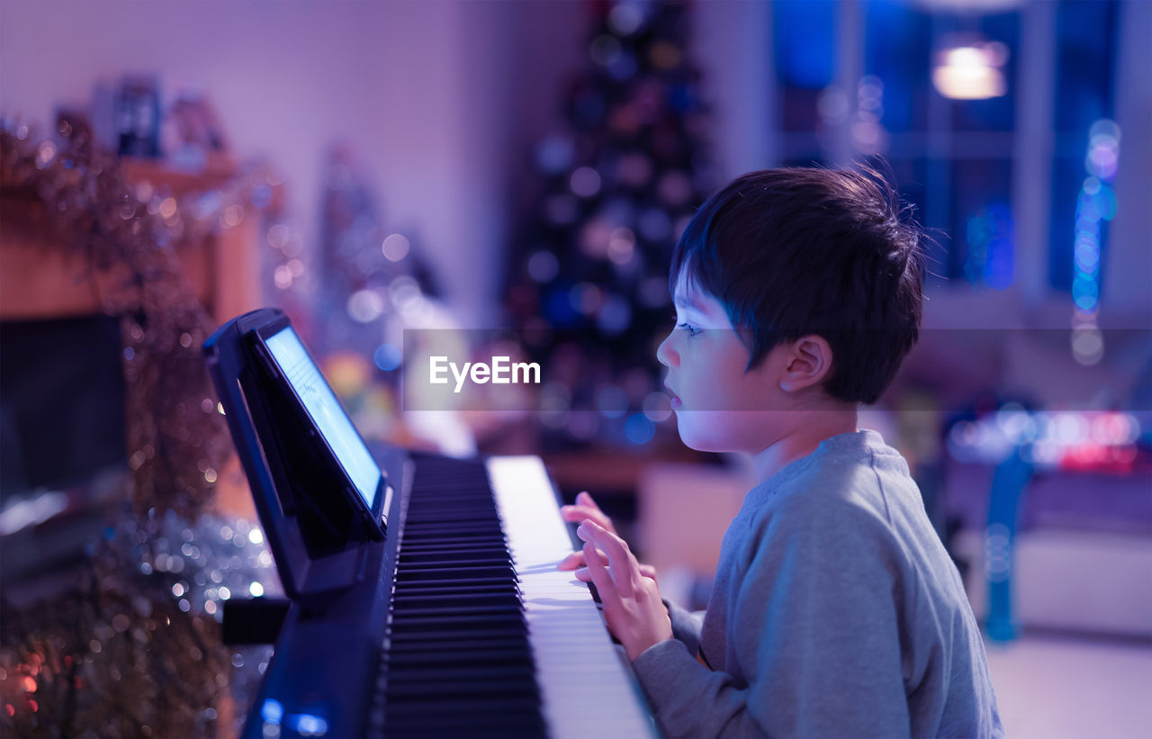 Side view of boy playing piano at home