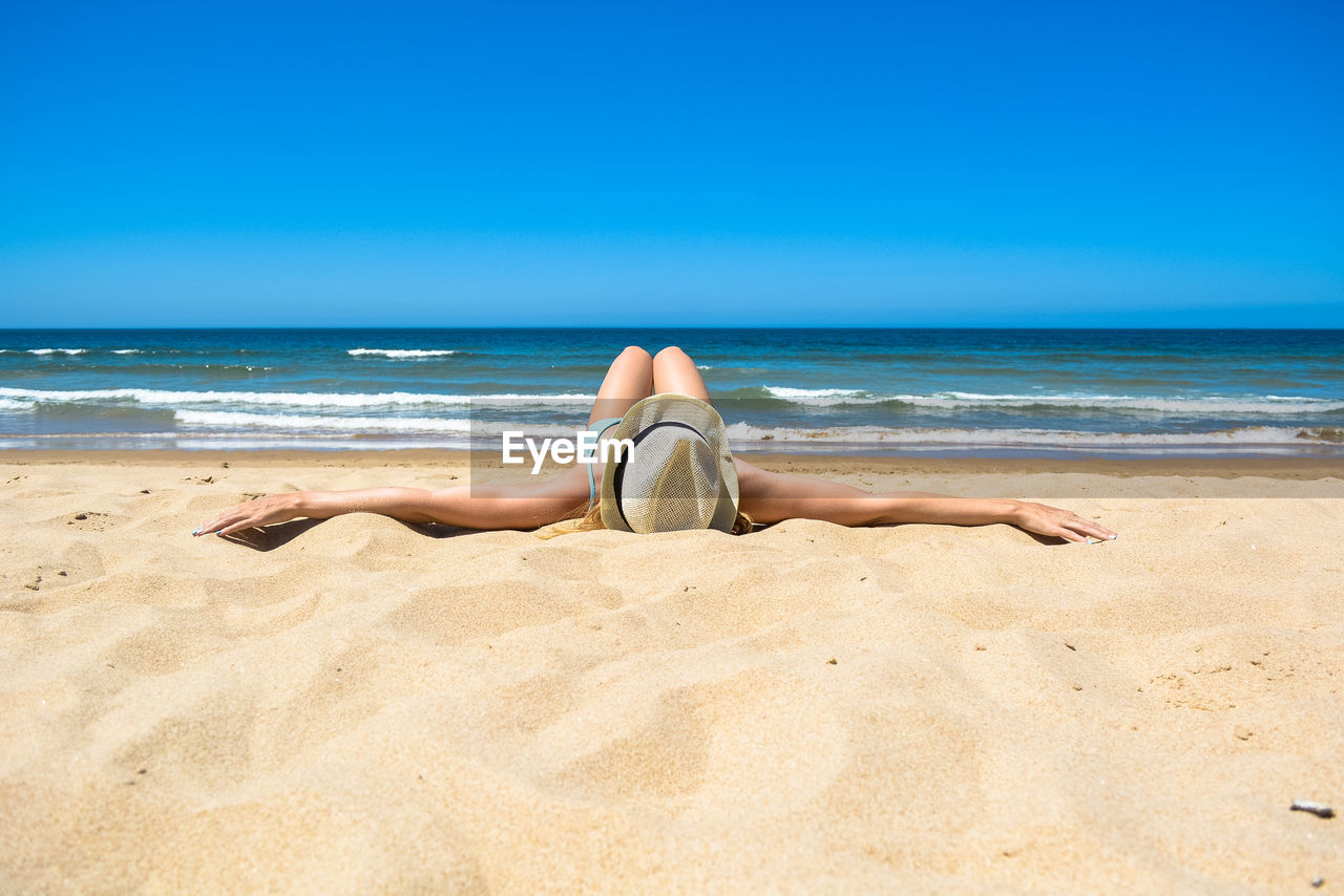 Woman lying on beach against blue sky