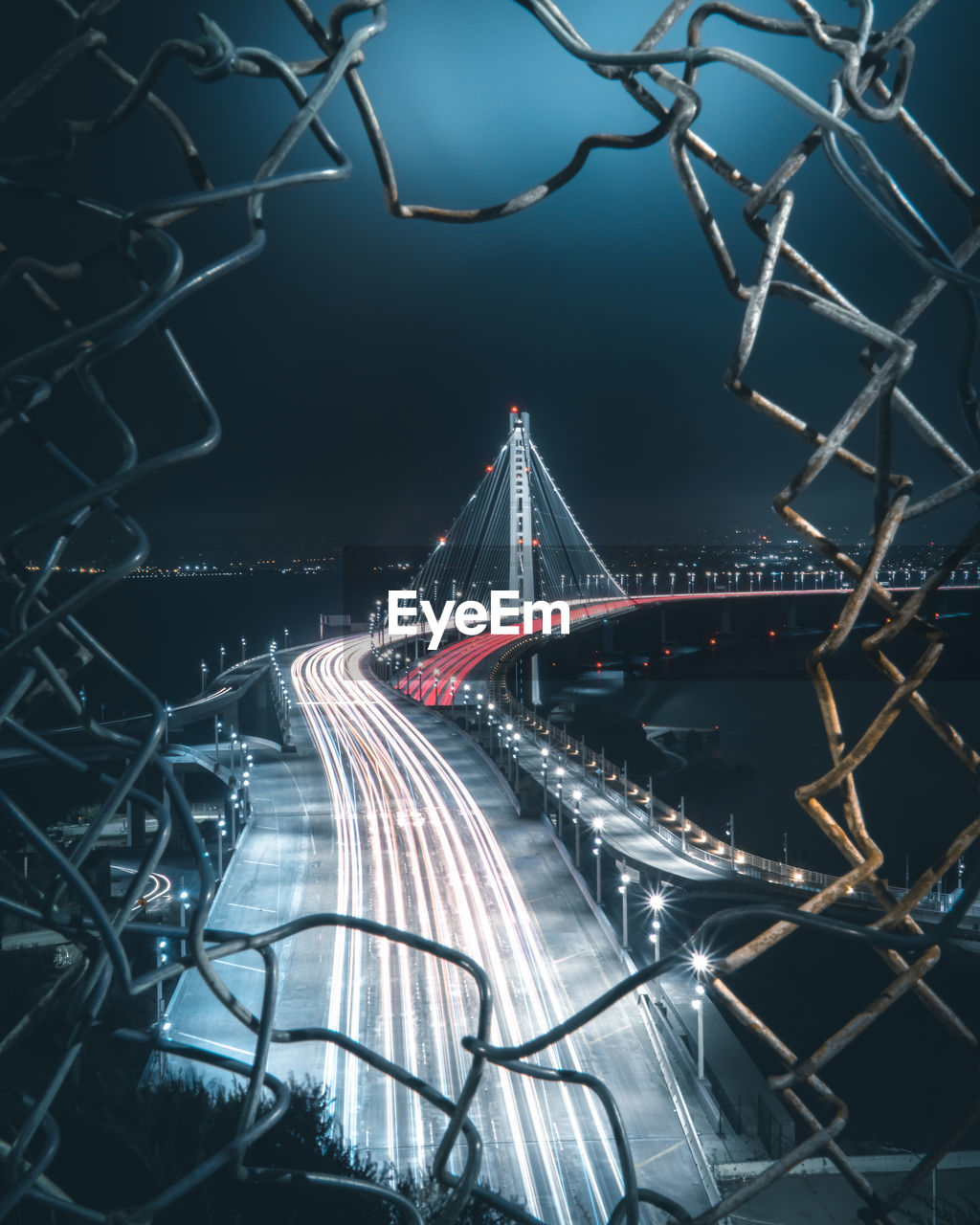 High angle view of light trails on bridge seen through hole in fence