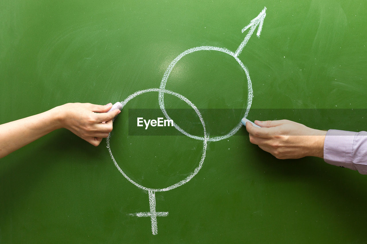Male and female hands draw symbols of masculine feminine principle with chalk on the blackboard. 