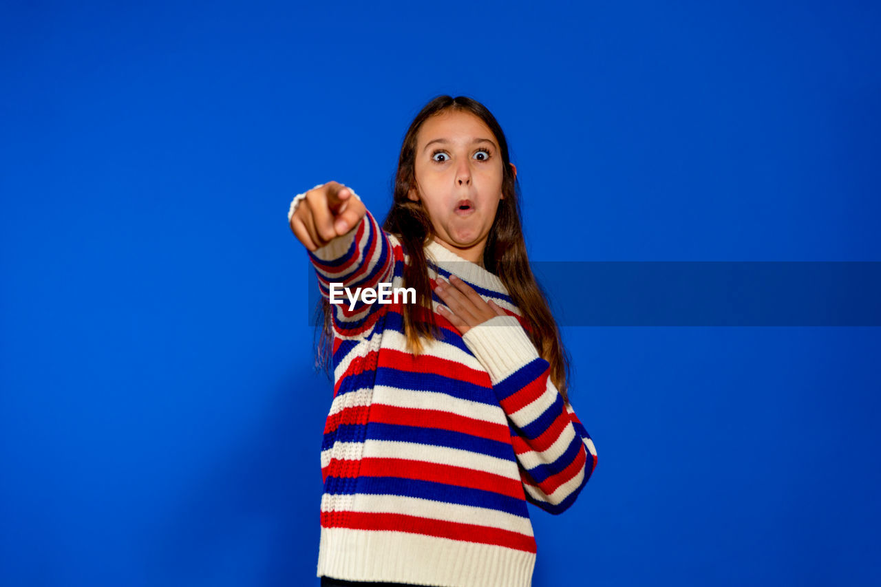 blue, one person, striped, studio shot, colored background, portrait, looking at camera, copy space, blue background, waist up, women, standing, young adult, child, clothing, casual clothing, emotion, photo shoot, person, front view, indoors, childhood, hairstyle, happiness, looking, adult, smiling, long hair, looking up, brown hair, lifestyles, human face, fun