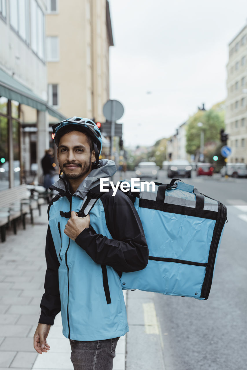 Portrait of smiling delivery man on sidewalk in city