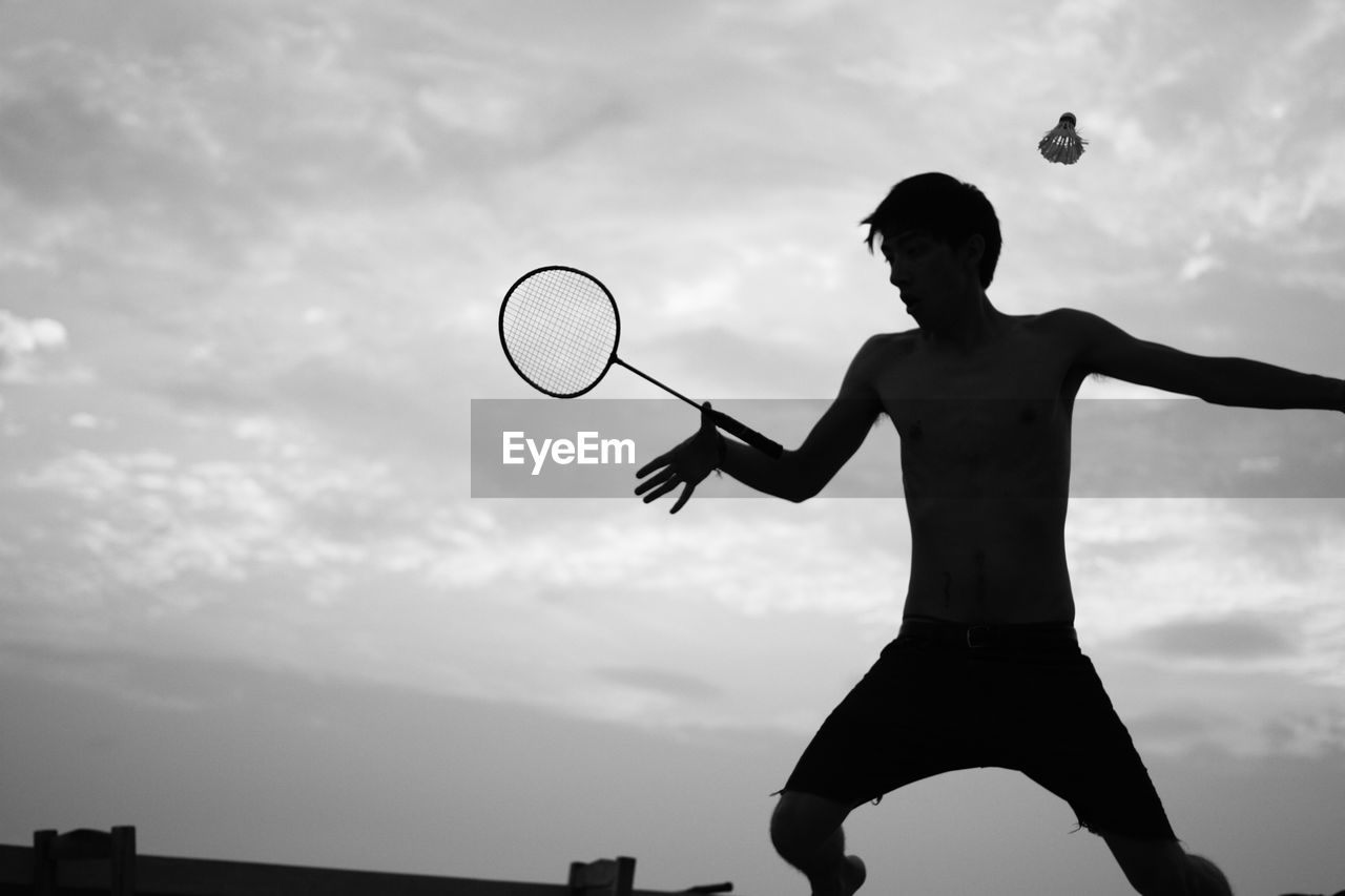 Shirtless man playing badminton against sky