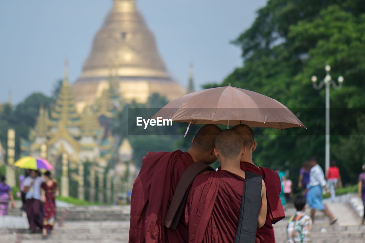 Rear view of monks under umbrella standing at shwedagon pagoda