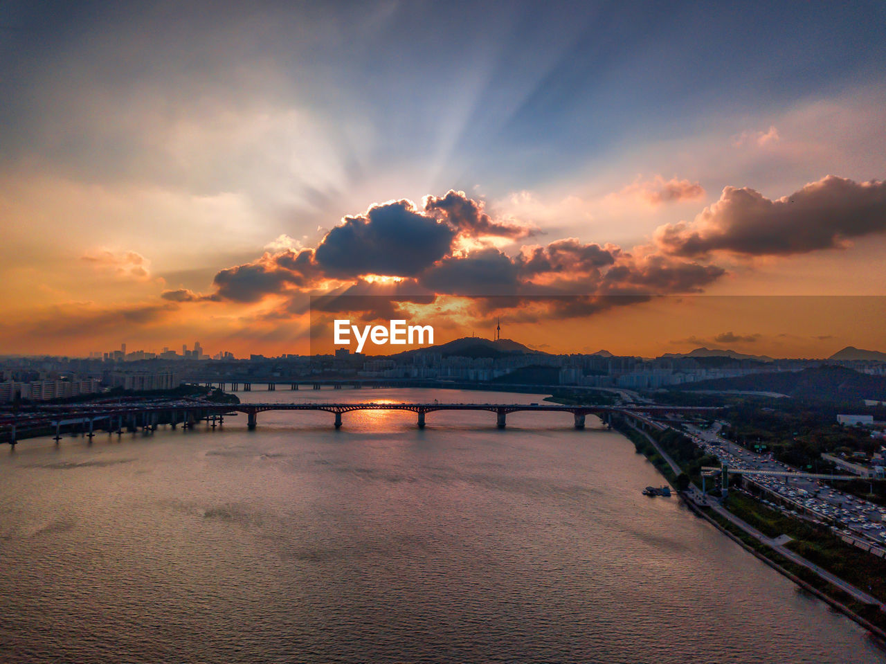 BRIDGE OVER RIVER AGAINST SKY IN CITY DURING SUNSET