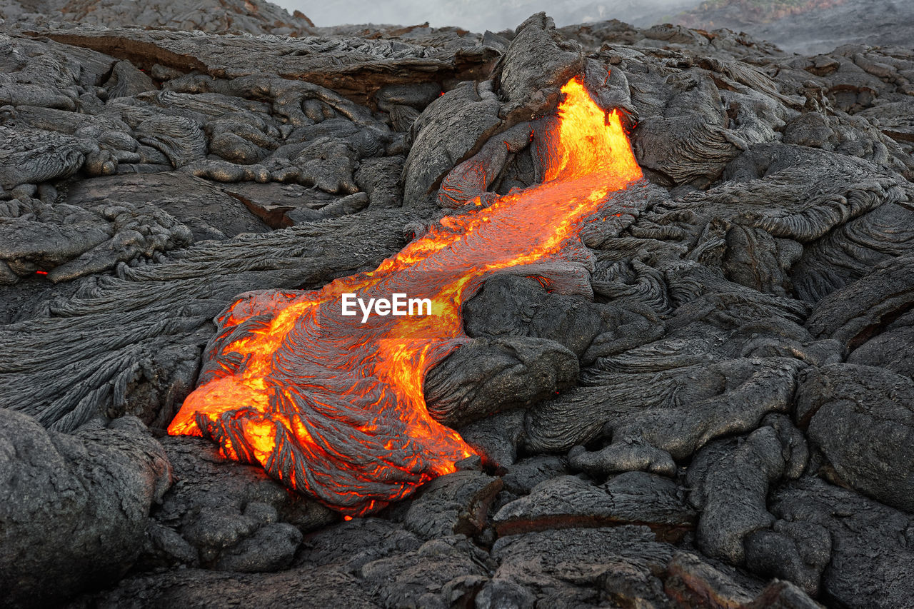Hot magma of an active lava flow emerges from a rock fissure, glowing lava makes the air flicker