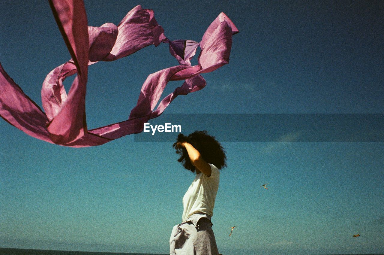 Woman standing by pink flowers against blue sky