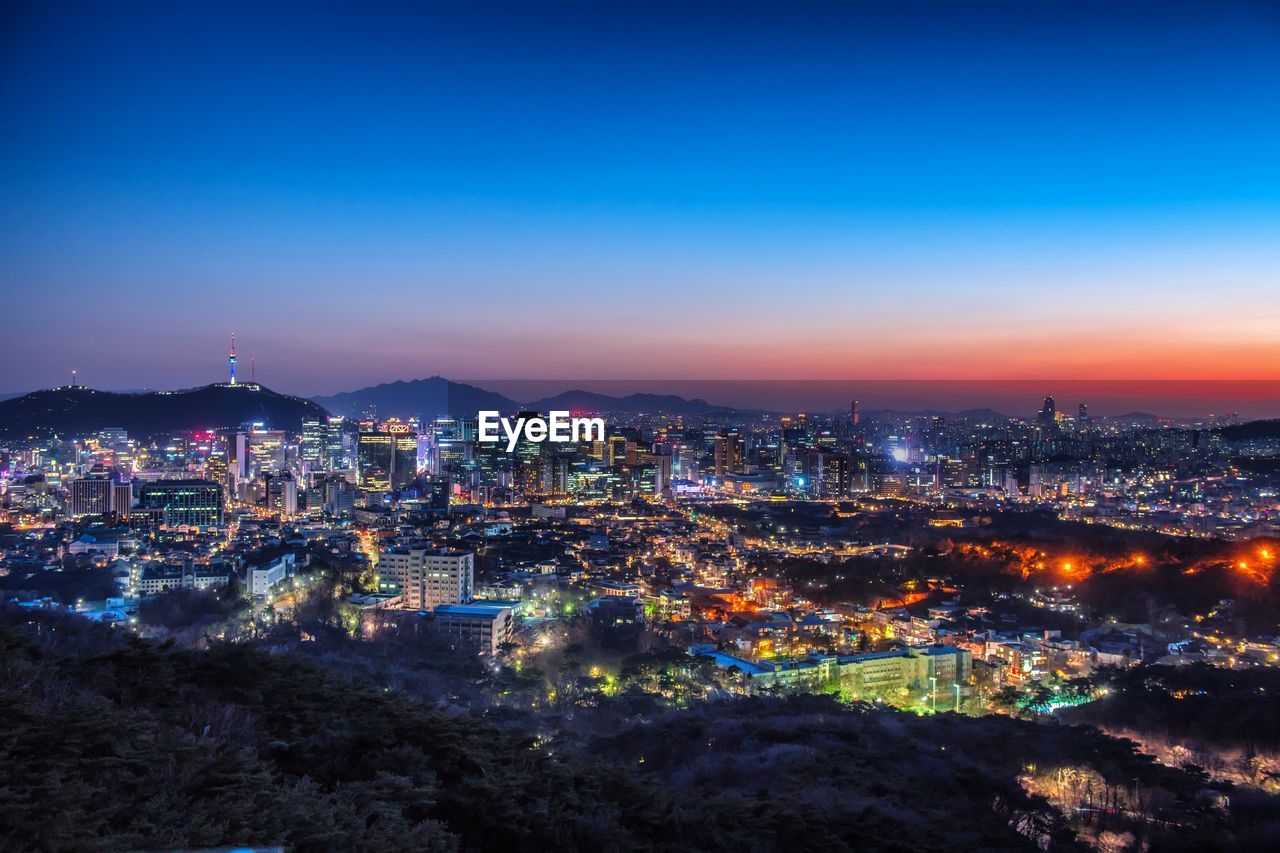 Aerial view of illuminated cityscape against blue sky during sunset