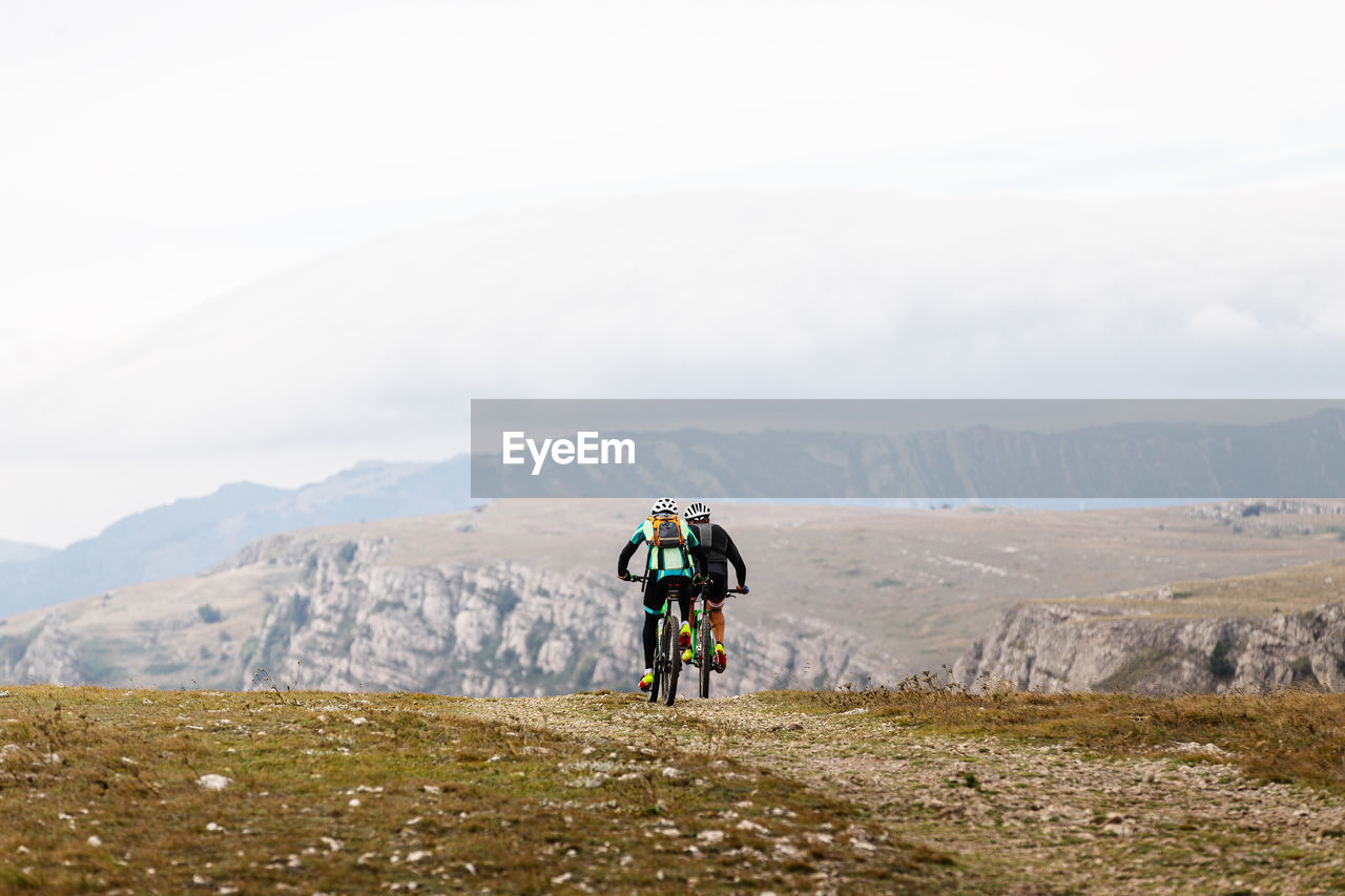 People riding bicycle on mountain against sky