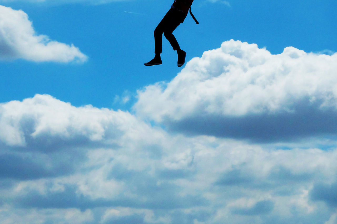 Low section of a man jumping against sky