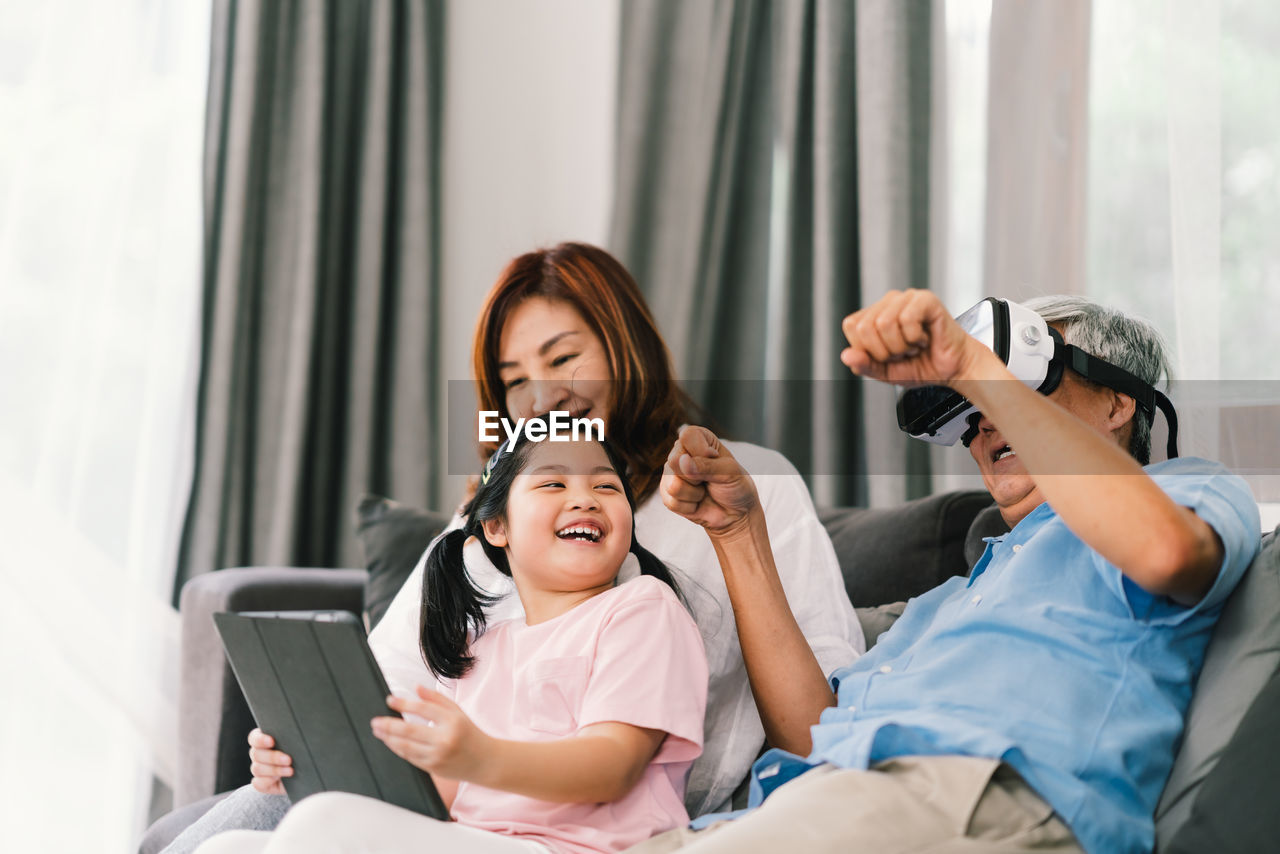 Smiling family using technologies while sitting on sofa