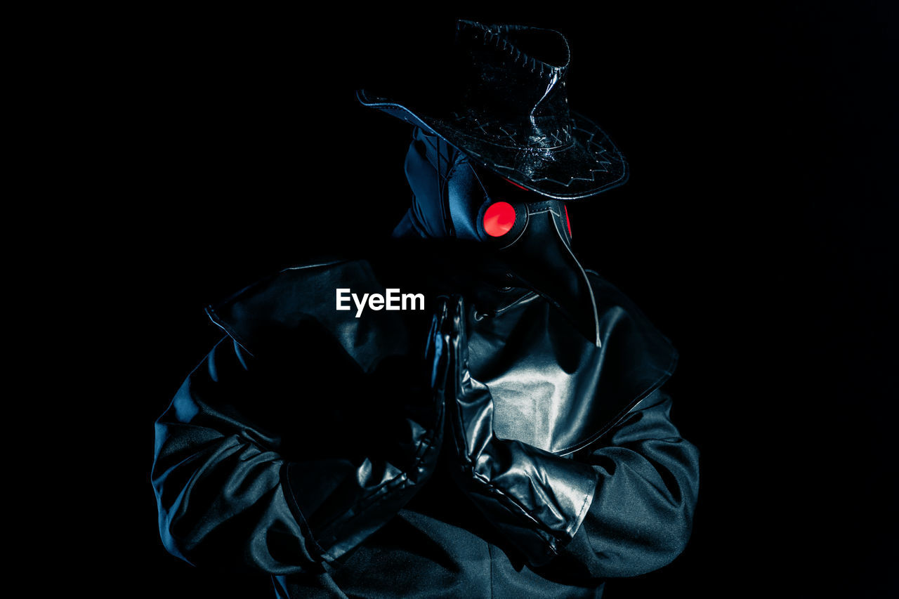 MIDSECTION OF MAN WEARING MASK AGAINST BLACK BACKGROUND AT NIGHT