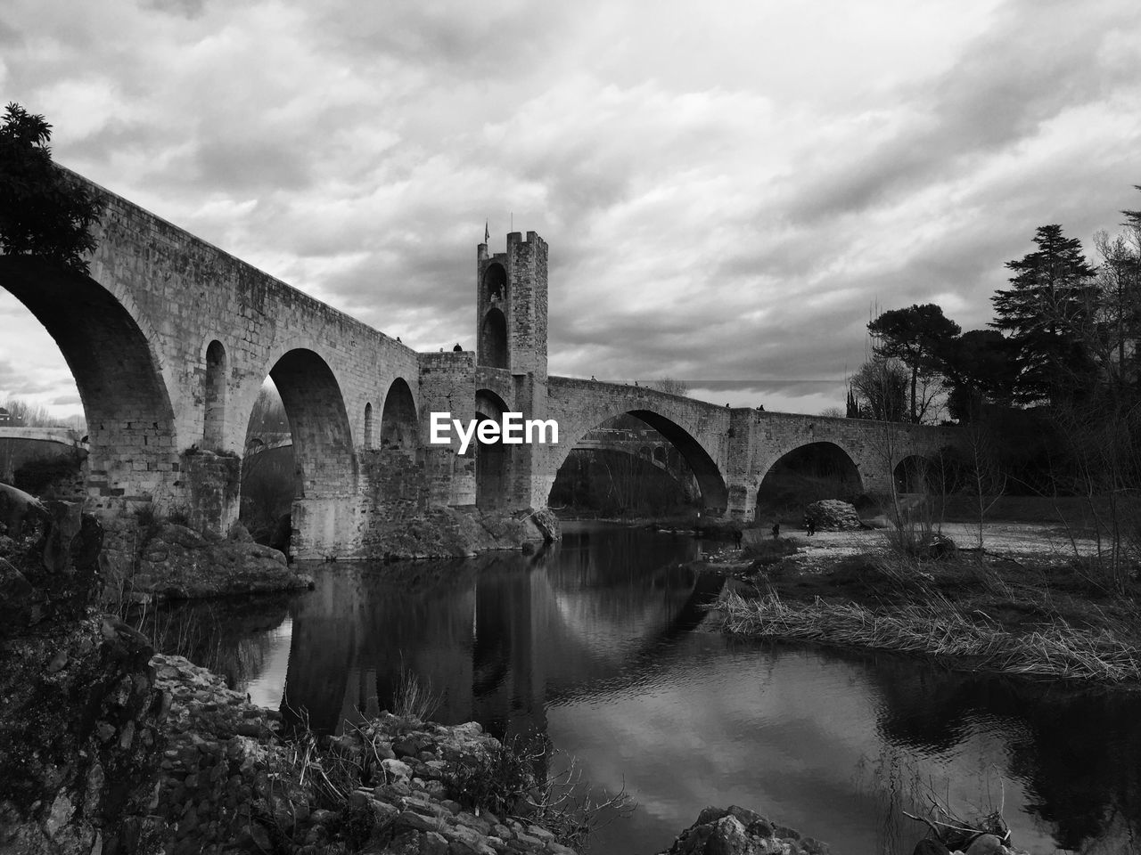 Low angle view of romanesque bridge over river against cloudy sky