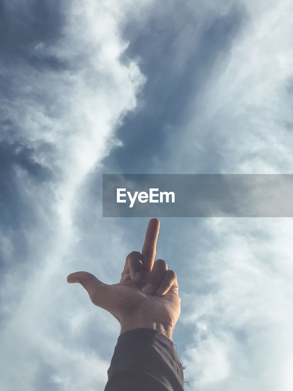 Cropped image of hand showing obscene gesture against cloudy sky
