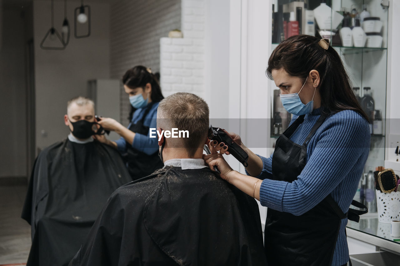 Female barber cutting hair of customer in saloon
