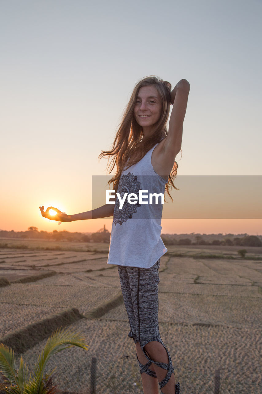 Optical illusion of teenage girl holding sun against sky during sunset