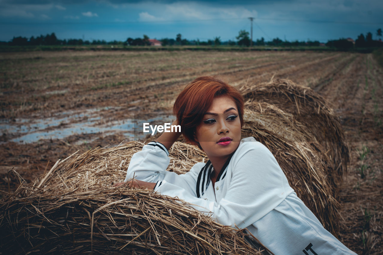 Thoughtful woman sitting on hay bale at field